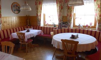 A cozy restaurant with bright walls and floral curtains. There are tables with white tablecloths and red benches against the wall.