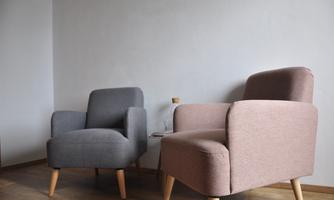 Two modern armchairs in soft colors are placed on a wooden floor. The wall in the background is simple and bright.