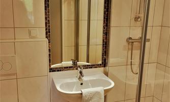 A modern bathroom with a sink, a mirror, and a shower cubicle. The walls are tiled, and the furnishings appear clean and functional.