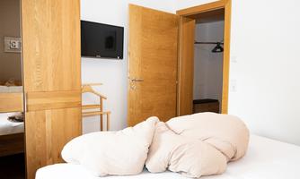 A cozy bedroom with a large bed and a television on the wall. The wooden details and the open doors create an inviting atmosphere.