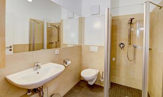 A modern bathroom with a shower, a sink, and a toilet. The walls are painted in light colors and there are large mirrors.