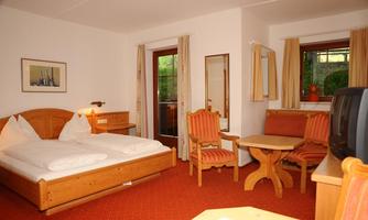 A cozy hotel room with a double bed, a table, and chairs. Large windows provide plenty of daylight and a view outside.
