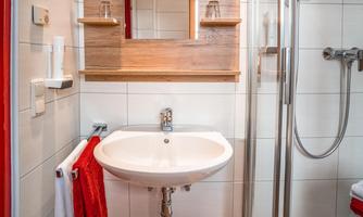 A modern bathroom with a shower, a sink, and a large mirror. The wall design is bright, while decorations in red add accents.