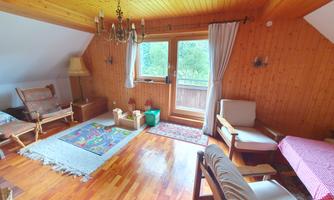 A cozy room with wooden paneling, a carpet, and several seating options. Large windows let in plenty of light and offer a view of nature.