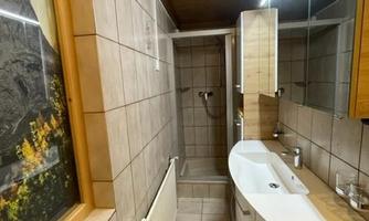 A modern bathroom with bright tiles and a curved sink. There is a shower and wooden elements that create a cozy atmosphere.