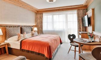 An elegant bedroom with a comfortable bed and warm color tones. There is a small table with chairs and large windows that let in plenty of light.