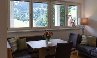 A cozy living area with a dining space and a view of the green landscape. Large windows let in plenty of light and offer a beautiful view of nature.