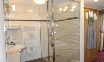A modern bathroom with a spacious glass shower and a sink. A traditional costume hangs on the wall.