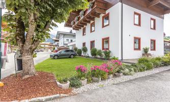 A well-kept house with white walls and red window frames. The garden is beautifully landscaped with colorful flowers and a green lawn.