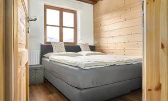 A cozy bedroom with a large double bed and wooden walls. The window lets in natural light and offers a beautiful view.