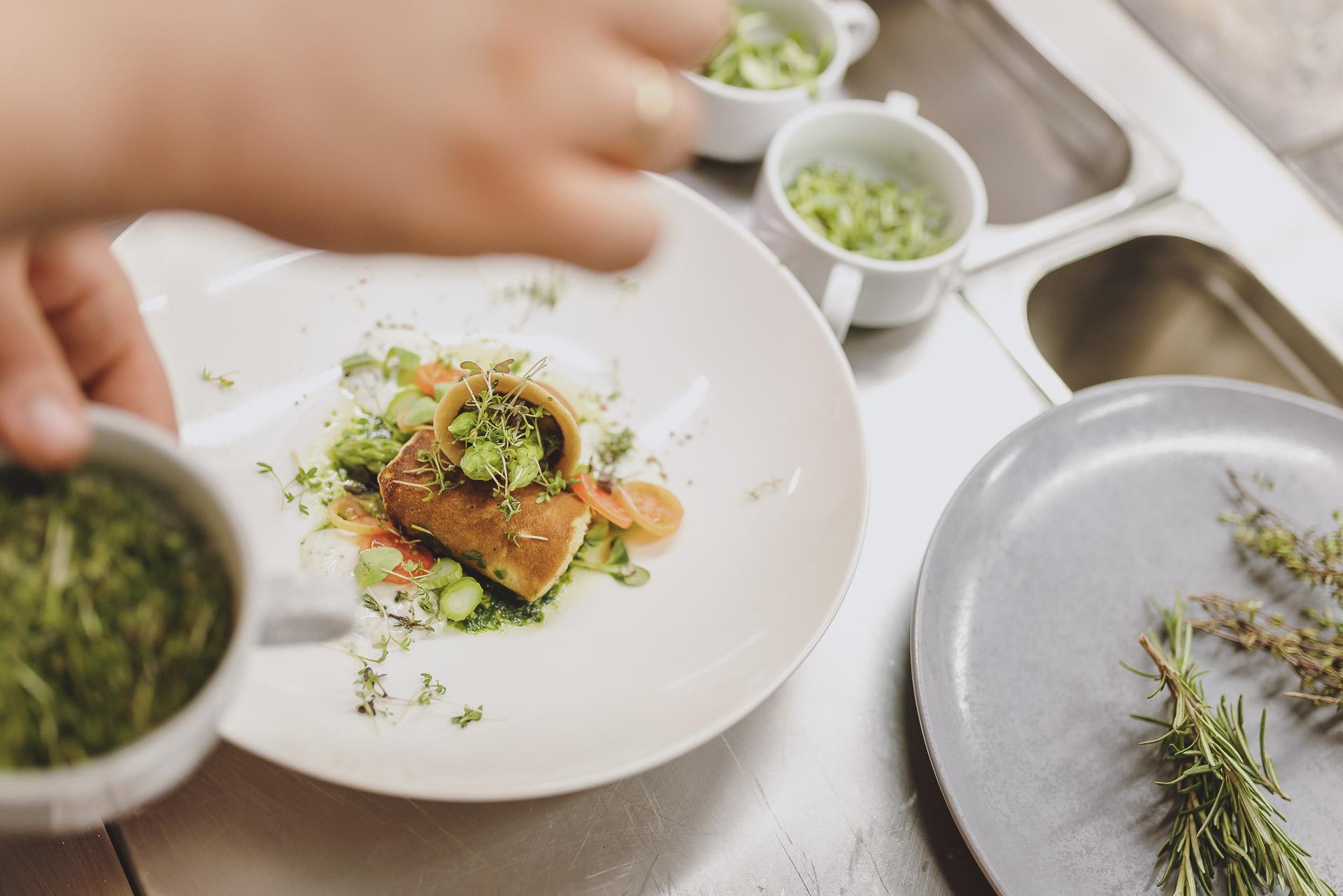 A plate with artistically arranged food, garnished with fresh herbs. In the background, bowls with additional ingredients are visible.