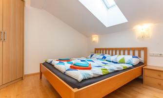 A cozy bedroom with a double bed and a large window. There is a wooden wardrobe and colorful bedding.