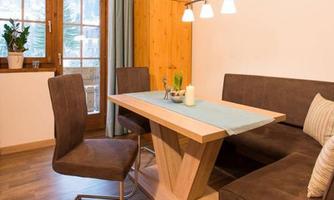 A cozy dining area with a wooden table and modern chairs. The windows offer a view of nature, and the decor is simple and inviting.