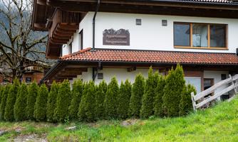 A building with a guesthouse sign and a well-kept hedge. The surroundings are green and rural.