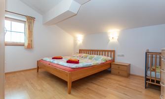 A bright bedroom with a large bed and a children's bed. The walls are white and the floor is made of wood.