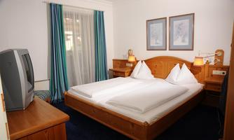 A cozy bedroom with a double bed and two pillows. The room has a television, a desk, and decorative pictures on the wall.