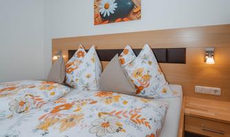 A cozy bedroom with a double bed and floral bedding. A decorative picture with floral motifs hangs on the wall.