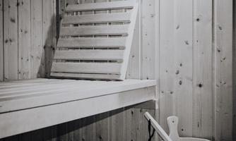 A simple sauna area with a wooden bench and a bucket. The walls are made of light wood and create a relaxed atmosphere.