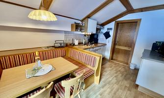 A cozy kitchen area with a wooden dining space and colorful benches. The modern decor and large windows create a bright, inviting atmosphere.