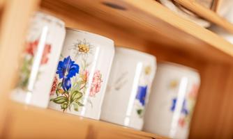 Various decorative cups with floral patterns are placed on a wooden shelf. The cups are made of porcelain and have different designs.