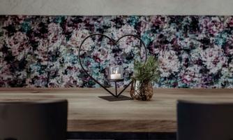 An elegant table with a heart-shaped candle holder and a small plant. In the background, there is a decorative wall with colorful patterns.