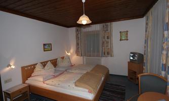 A cozy bedroom with two beds, wooden ceiling, and inviting colors. The room is simply furnished, with a chair and a television in the corner.