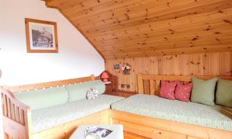 A cozy attic room with wooden walls and a rustic seating area. The sofas are decorated with checkered cushions and there is a small table in the middle.