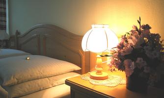 A cozy bedroom with a double bed and a nightstand. On the nightstand, there is a table lamp and a flower arrangement.