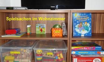 A living room with a television and toys on a shelf. The toys are organized in transparent boxes.