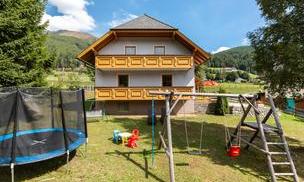 A beautiful house with a large garden. In the garden, there is a trampoline and a swing for children.