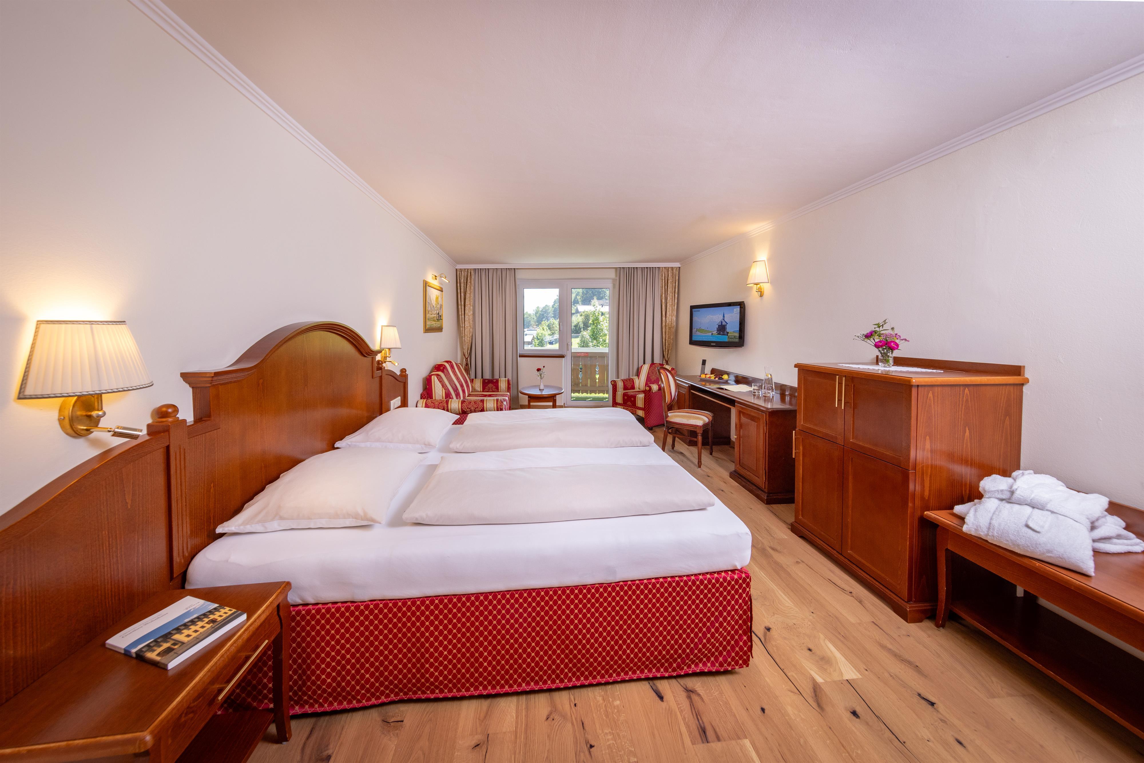 A comfortable hotel room with two single beds, cozy seating, and natural light. The space is simply but invitingly furnished.