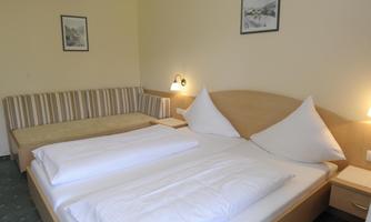 A cozy bedroom with a double bed and a couch. The walls are in soft colors, and there are decorative pictures.