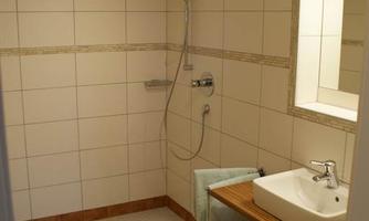A modern bathroom with a shower and a sink. The walls are brightly tiled, and the floor is in a warm earth tone.