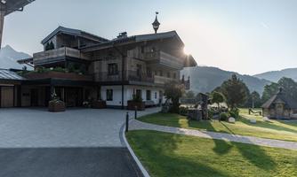 An elegant wooden house in the mountains with a green lawn. The sun is shining, giving the surroundings a warm atmosphere.