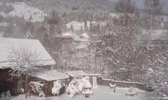 A snowy landscape with houses and trees. The surroundings are covered by a thick layer of snow, creating a winter atmosphere.