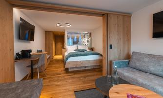 A modern hotel room with wooden paneling, a cozy bed, and an inviting living area. The decor is minimalist and stylish, with a touch of warmth.