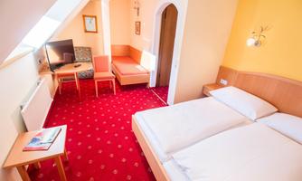 A cozy hotel room with a double bed and a small table. The walls are painted in warm colors, and the room is equipped with a television and a seating area.
