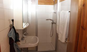 A bathroom with a shower and a sink. White tiles and wooden details give the room a pleasant atmosphere.