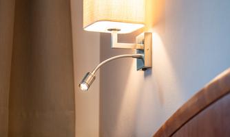 A modern wall lamp with a fabric shade that provides soft light. Next to the bed, it adds a cozy atmosphere.
