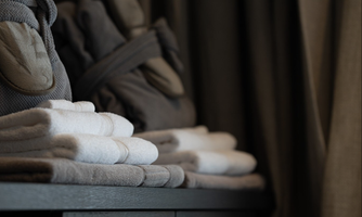 A stylish collection of towels and bathrobes on a wooden shelf. The background is surrounded by a curtain in an elegant design.
