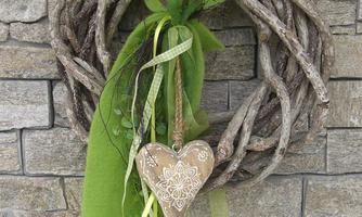 A decorative wreath made of twigs with a heart-shaped pendant. The wreath is adorned with green ribbons and a fabric bow.