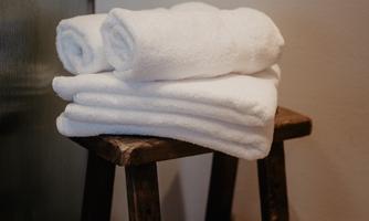 Five neatly rolled towels are lying on a wooden stool. The background is neutral and simple.