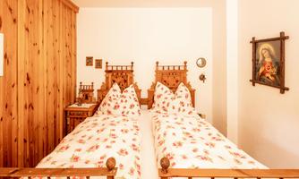 A cozy bedroom with two single beds and wood-paneled walls. The bedding is adorned with a floral pattern, and a picture on the wall depicts a religious figure.
