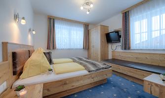 A bright room with a double bed and wooden furniture. The room is cozy and equipped with a television and a seating area.