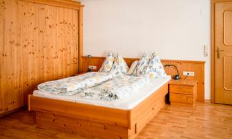 A cozy bedroom with a double bed and wooden paneling. The bedding is bright and floral patterned.
