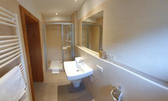 A modern bathroom with a shower, sink, and large mirrors. The walls are in light colors, and there is a towel rack.