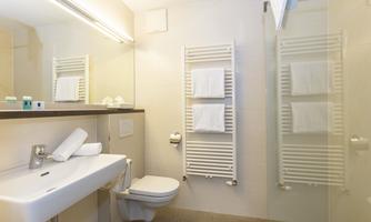 A modern bathroom with a sink, a toilet, and a glass shower. Towels hang on a towel rack.