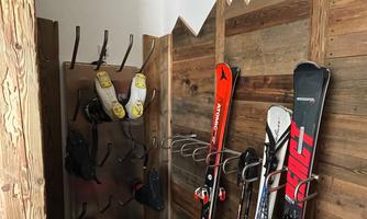 A ski room with skis on a wooden rack. Helmets and other ski equipment hang on the wall.