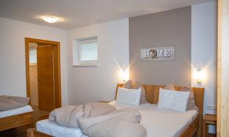A cozy bedroom with two beds and soft pillows. The walls are light, and a decorative wall plate with the word "HOME" gives the room an inviting atmosphere.