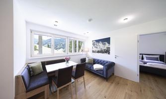 A modern living room with a table and cozy chairs. Large windows offer a view of the mountains.